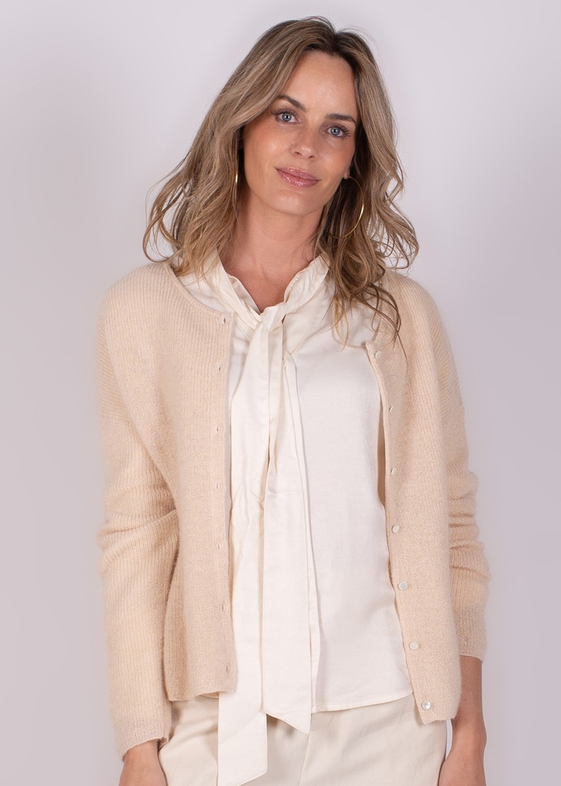 Model draagt een lichte Narvik cardigan over een crèmekleurige blouse met strik.