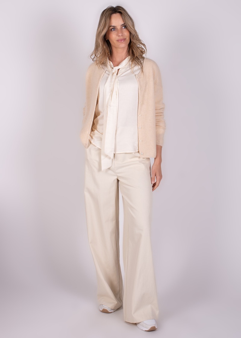 Model draagt een crèmekleurige Narvik cardigan met bijpassende blouse en wijde broek, gefotografeerd tegen een neutrale achtergrond.