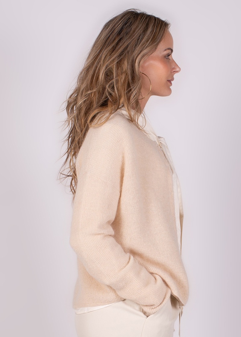 Een vrouw in zijaanzicht draagt een beige Narvik cardigan met haar handen in de zakken.