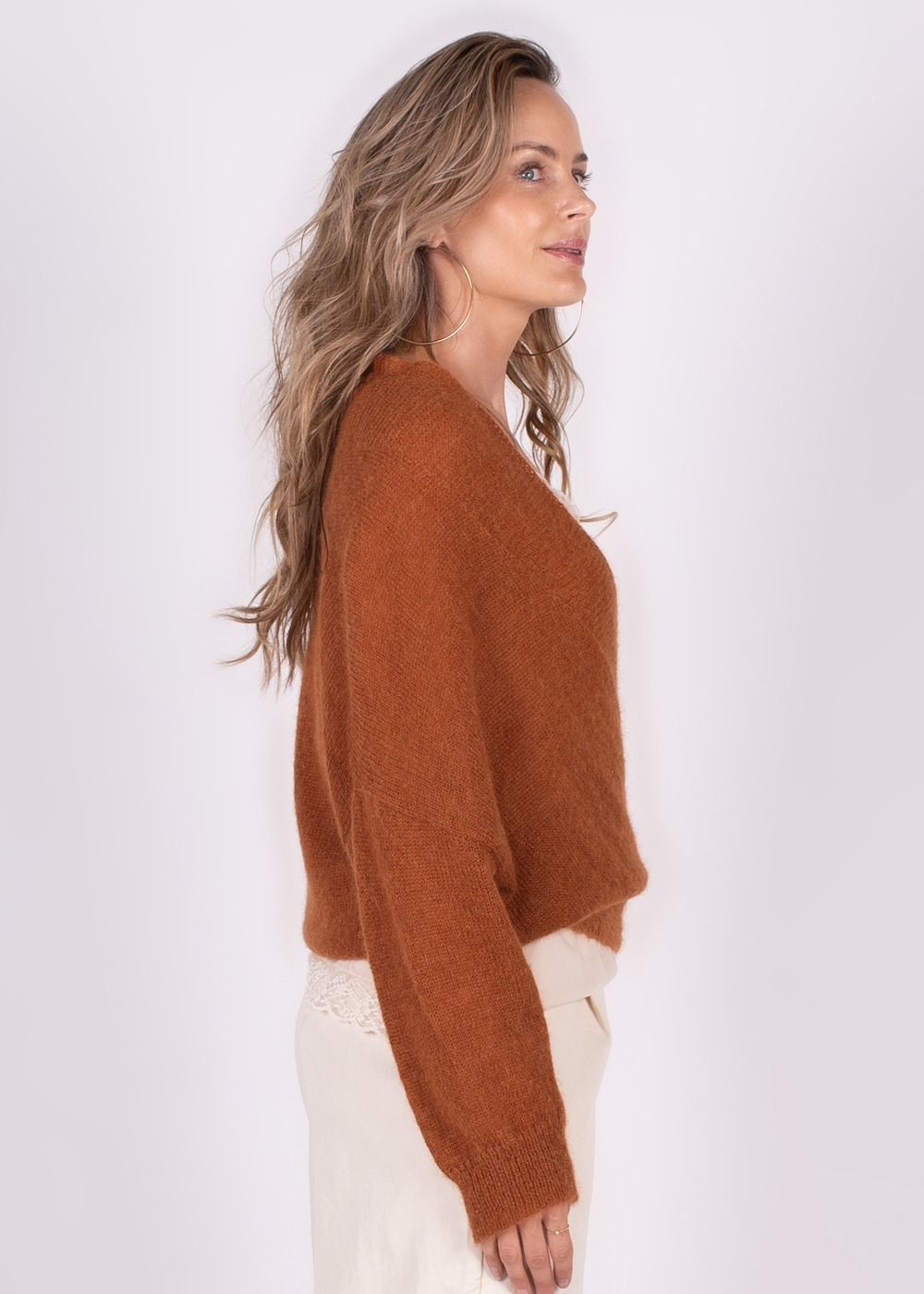 Model in een zijaanzicht draagt een roestkleurige Narvik overslag cardigan met lichte broek op een neutrale achtergrond.