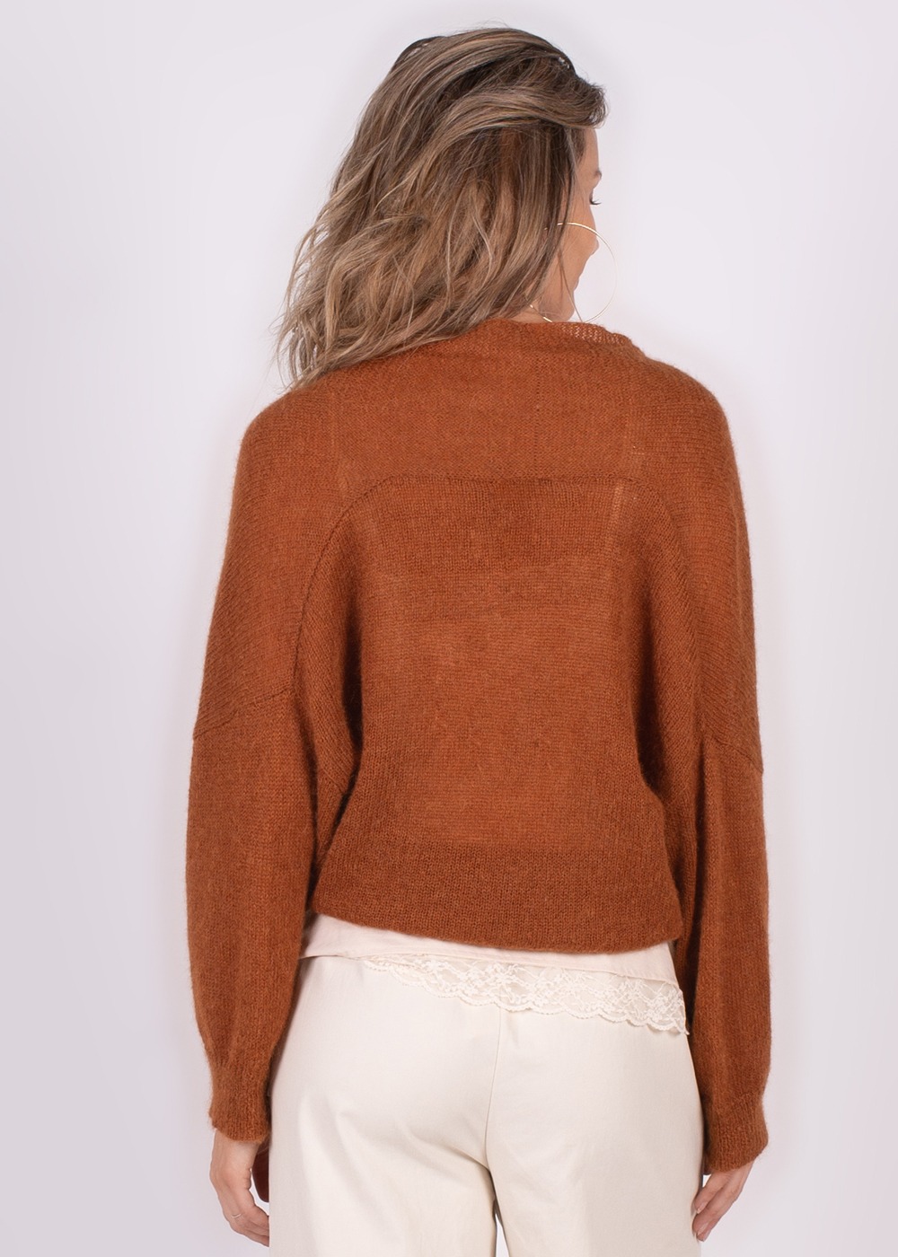 Achteraanzicht van een vrouw die een bruine Narvik overslag cardigan draagt, gecombineerd met een witte kanten top en lichte broek.