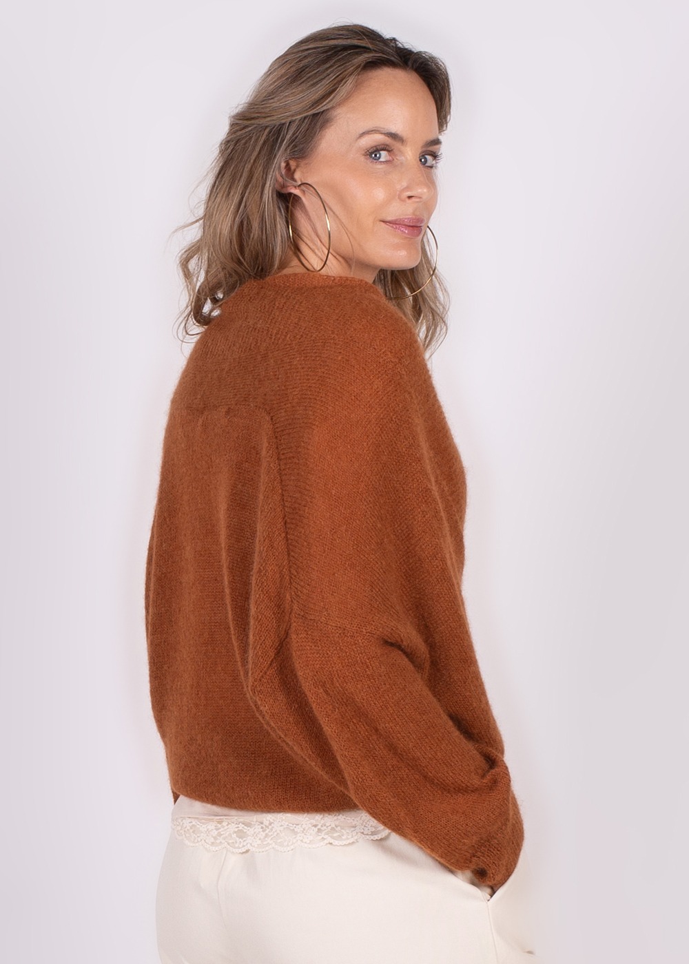 Model draagt een warmbruine Narvik overslag cardigan met kanten top eronder, gefotografeerd van achteren met het gezicht naar opzij.
