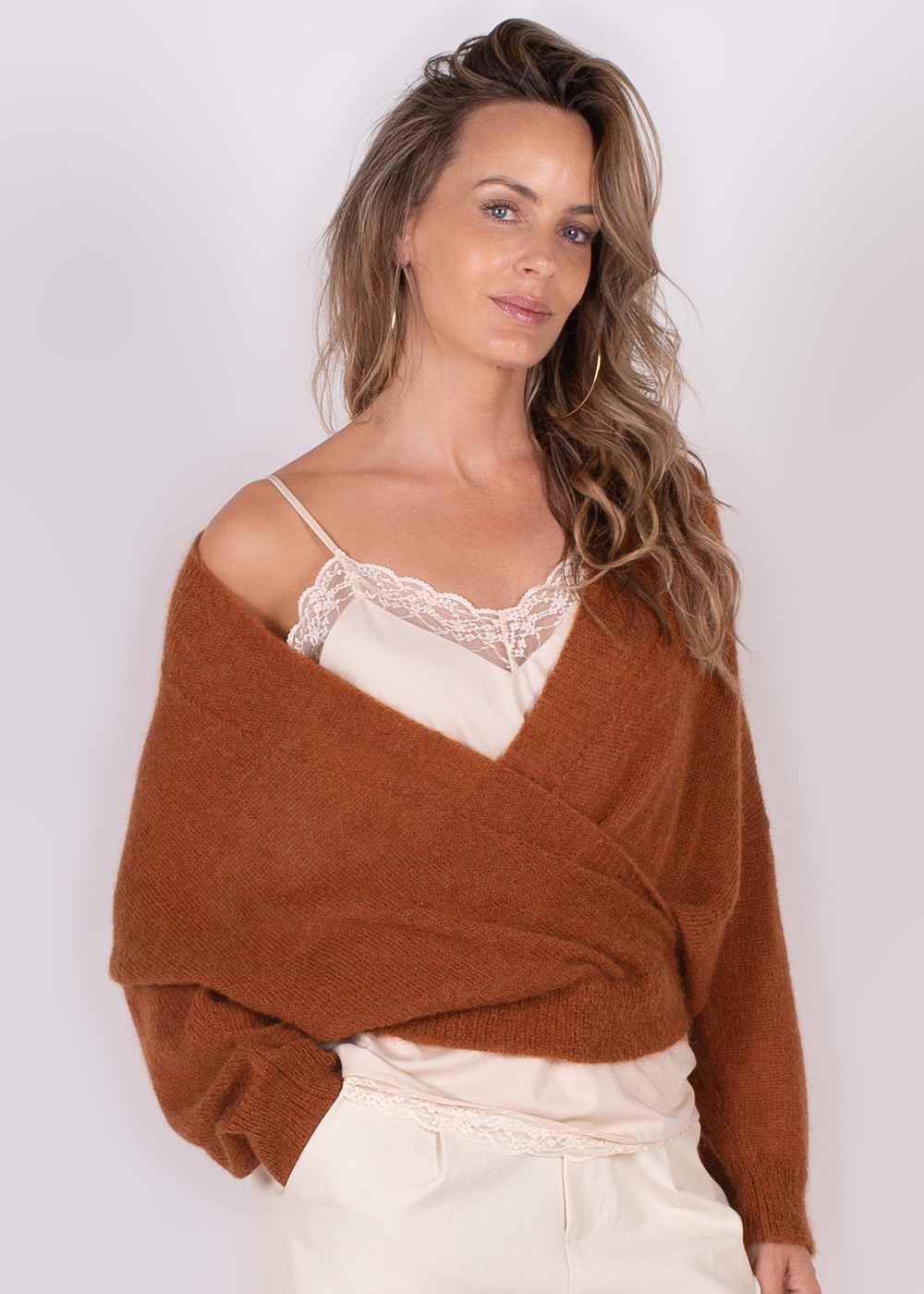 Een vrouw draagt een warme, bruinrode Narvik overslag cardigan over een lichte satijnen top.