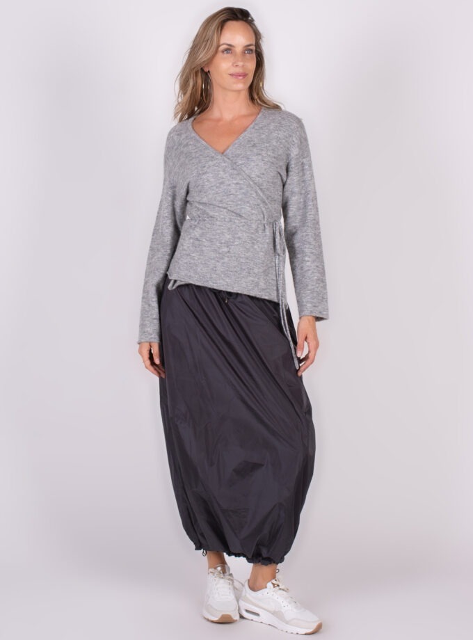 Een vrouw draagt een grijze Odense cardigan met een zwarte rok en witte sneakers, weergegeven in een volledige lichaamshoek.