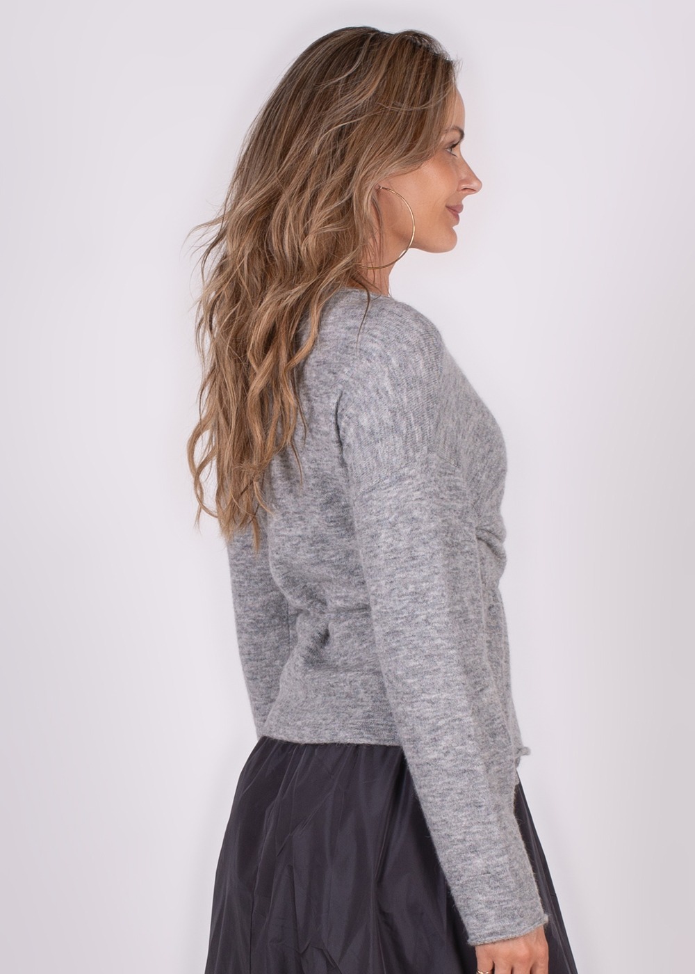 Zijaanzicht van een model dat een grijze Odense cardigan draagt, gecombineerd met een donkere rok.