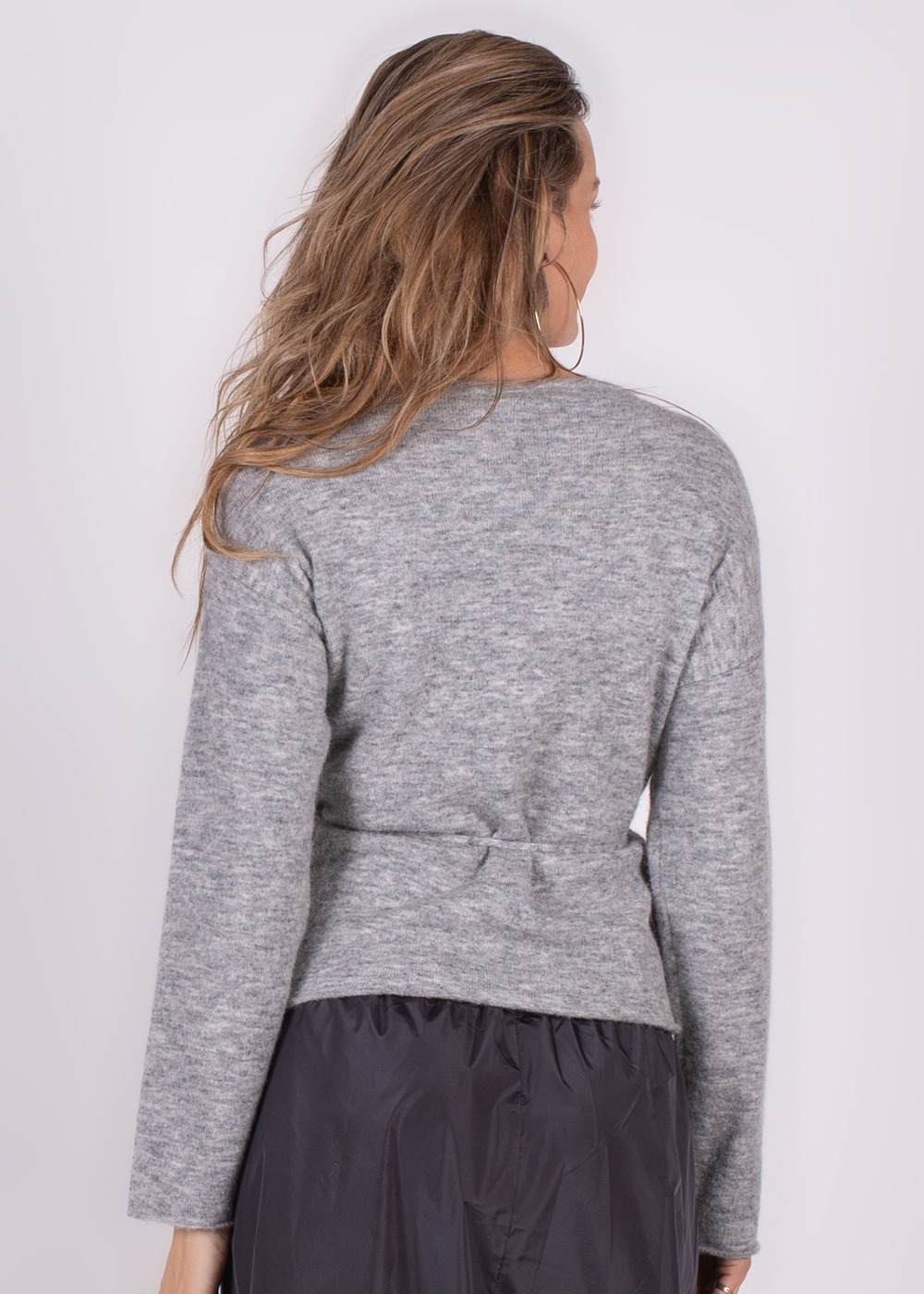 Achteraanzicht van een persoon die een grijze Odense cardigan draagt met losse haren en een zwarte rok.