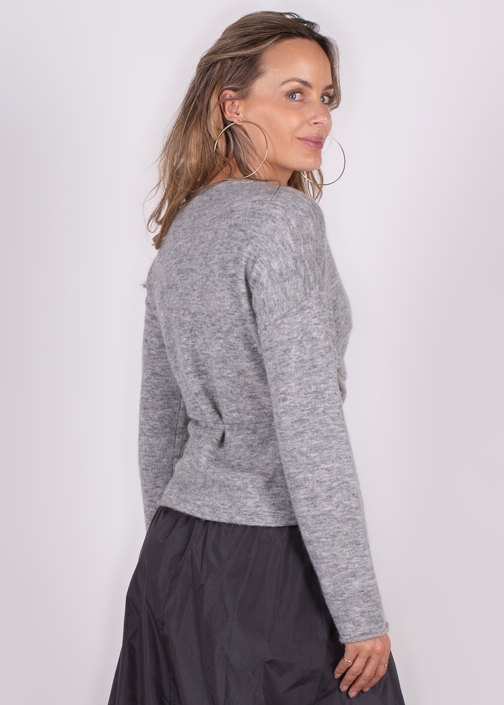 Model draagt een grijze Odense cardigan en kijkt over haar schouder naar rechts op een witte achtergrond.