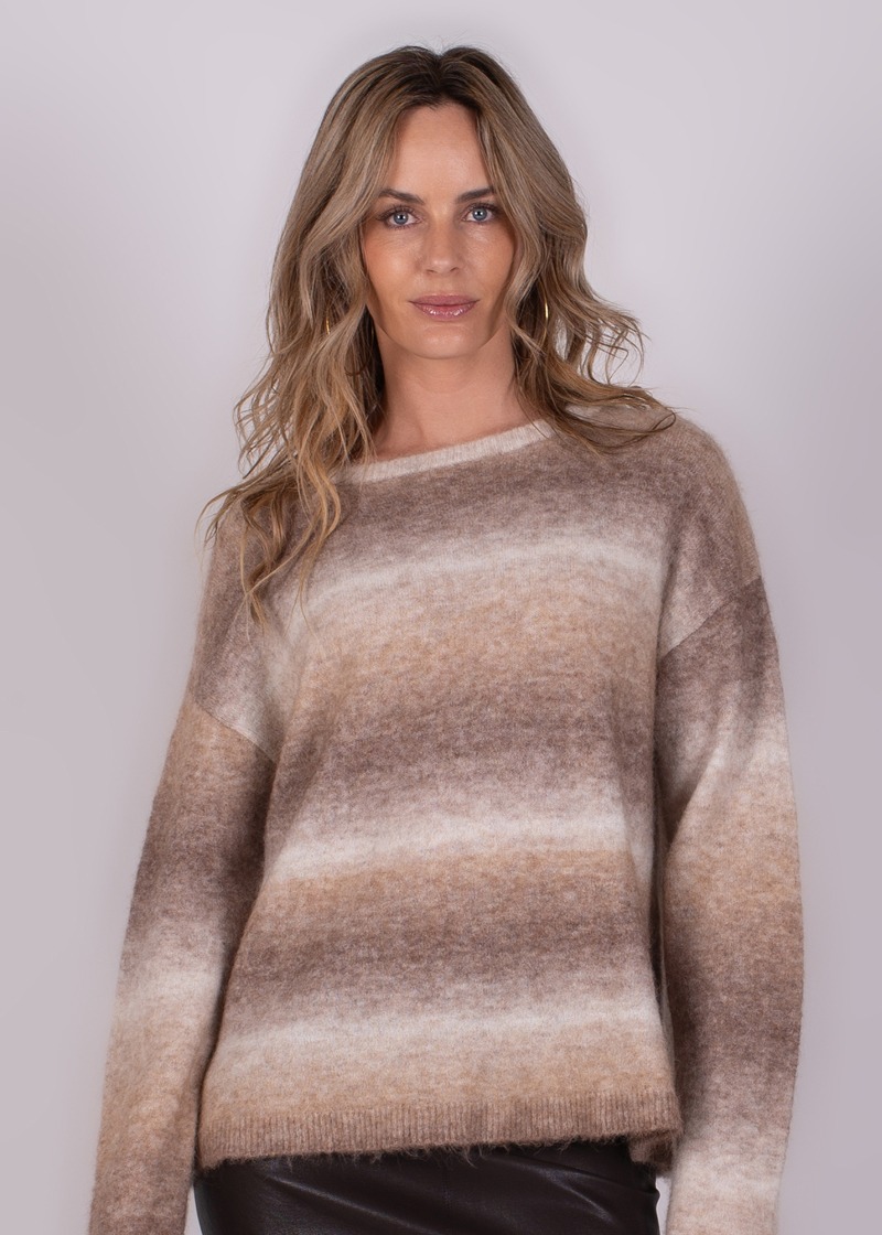 Vrouw in een bruin-beige gestreepte trui tegen een neutrale achtergrond, frontaal gefotografeerd.