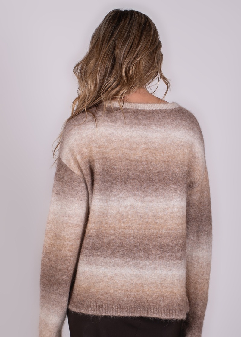 Model met halflang golvend haar gefotografeerd van achteren, draagt een trui met brede horizontale bruine en beige strepen.
