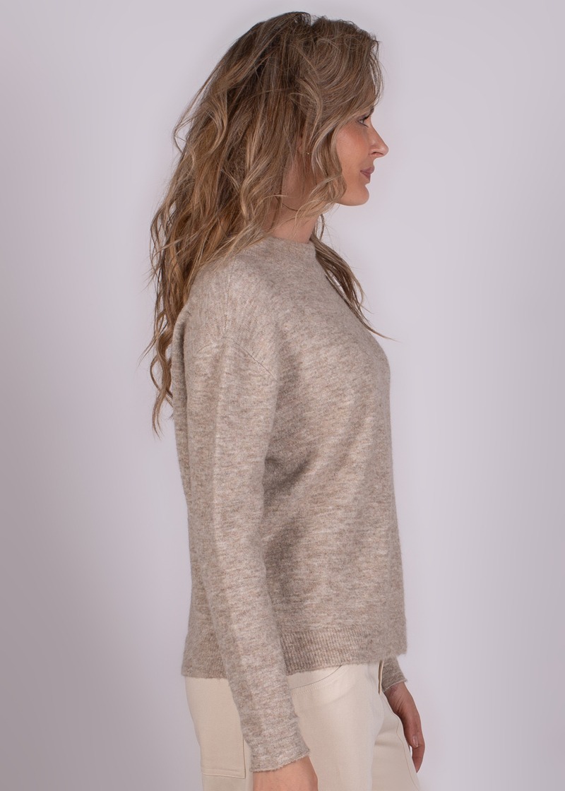 Zijaanzicht van een model dat een beige trui draagt tegen een neutrale achtergrond.