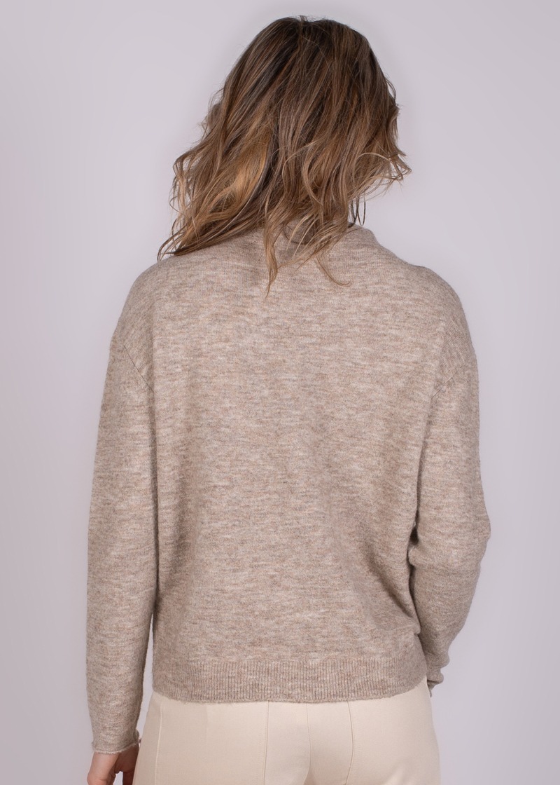 Achteraanzicht van een vrouw met los haar die een beige gemêleerde trui draagt tegen een lichtgrijze achtergrond.