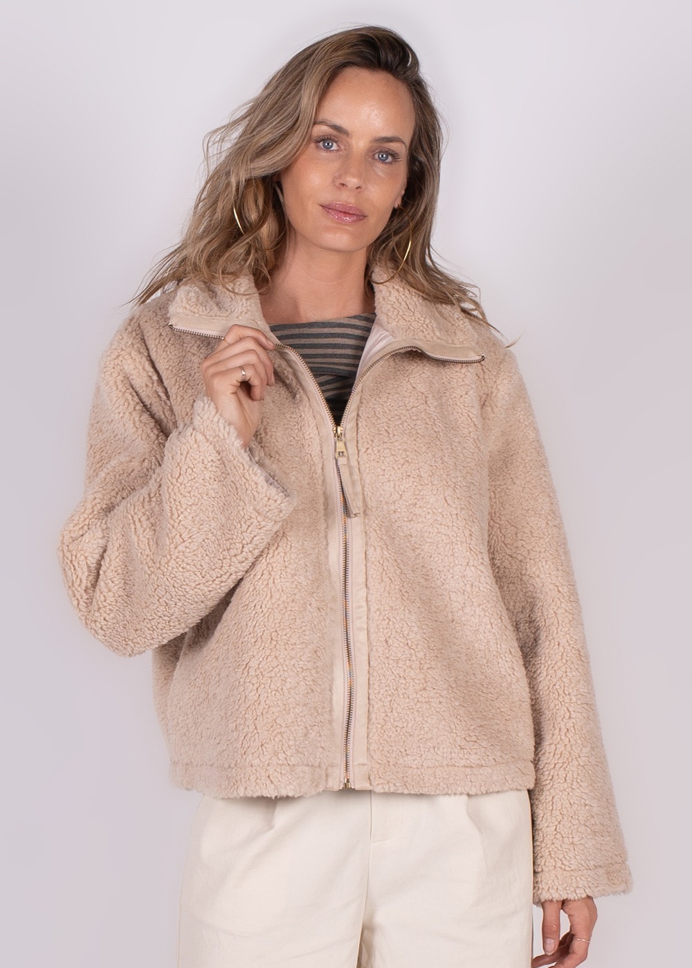 Een vrouw poseert in een crèmekleurige Regina gilet met een ritssluiting, gefotografeerd van voren tegen een neutrale achtergrond.