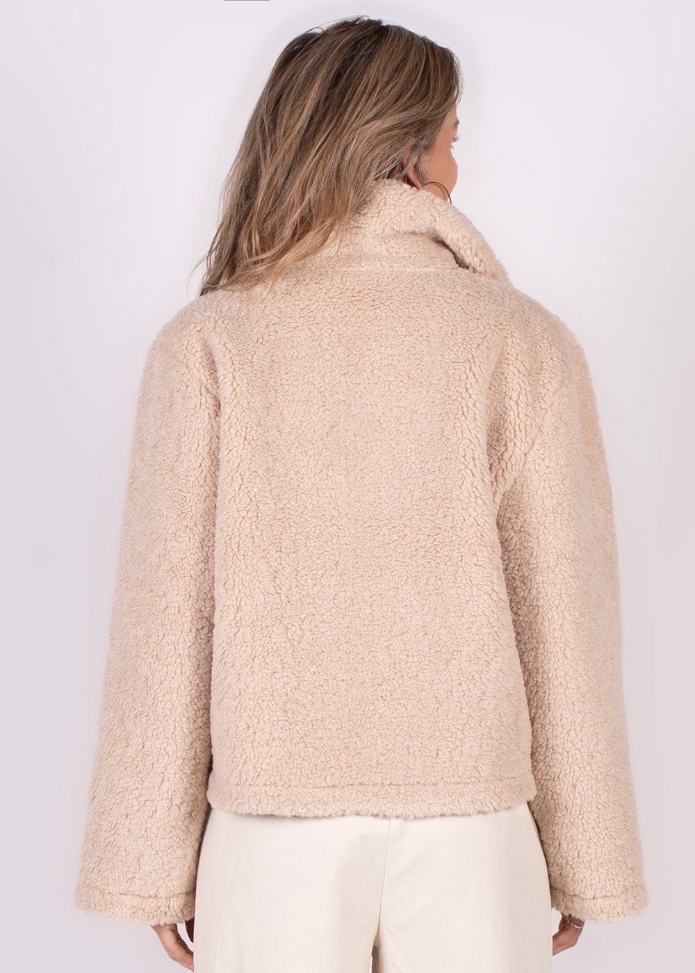 De achteraanzicht van een vrouw die een licht beige, teddy-achtige Regina gilet draagt.
