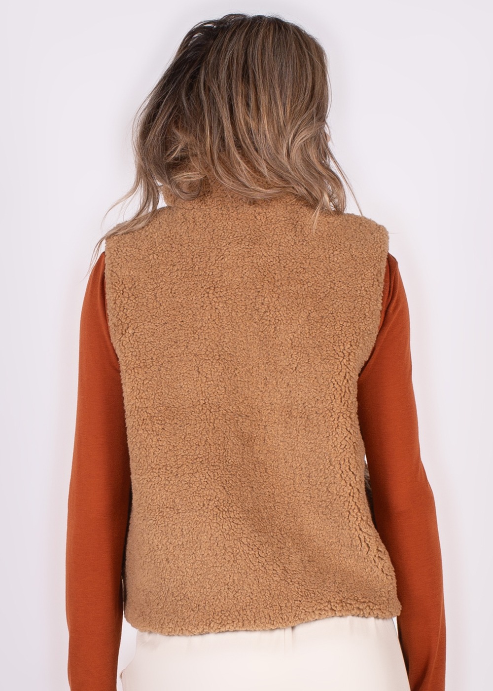Achteraanzicht van een persoon met een bruin, teddy gilet over een roestkleurige trui.