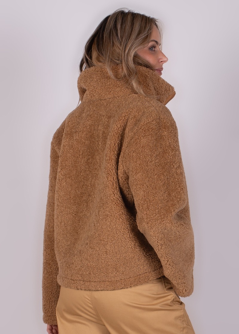 Een vrouw in een beige teddyjack, gezien van achteren met een half zijaanzicht.
