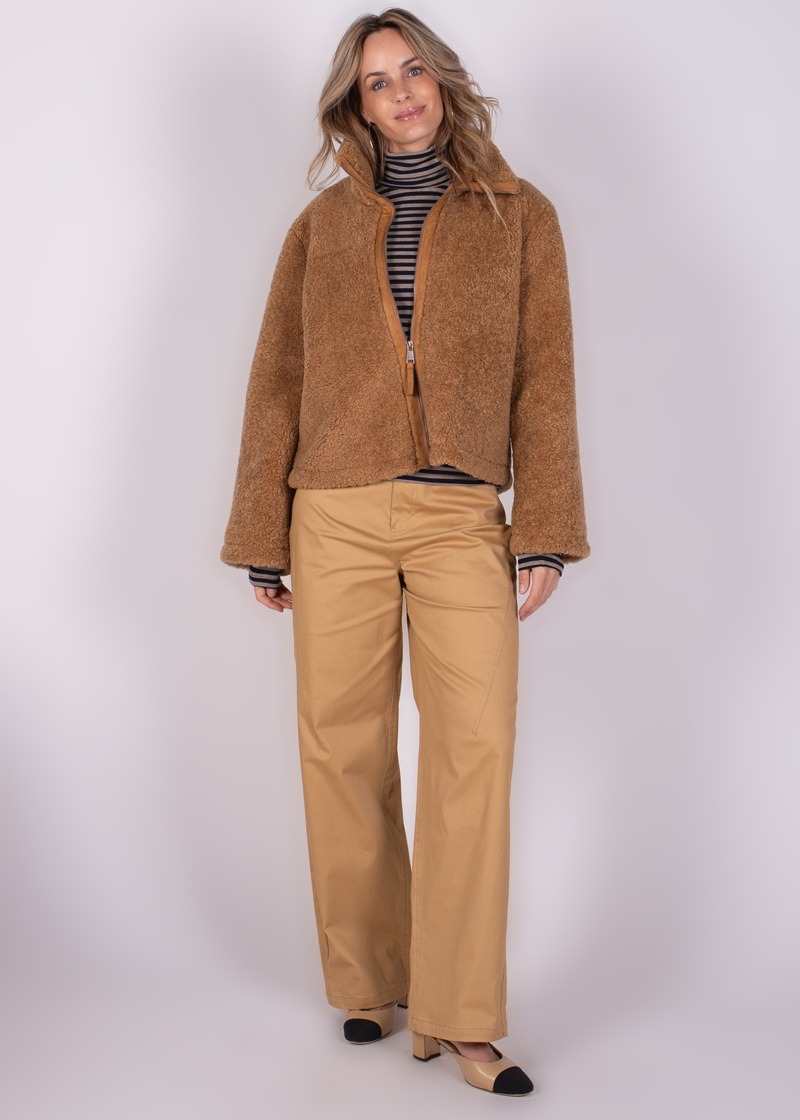 Een vrouw poseert in een bruine, wollen Regina jas met rits, beige broek en een gestreepte coltrui, gefotografeerd vanuit een frontaal perspectief.