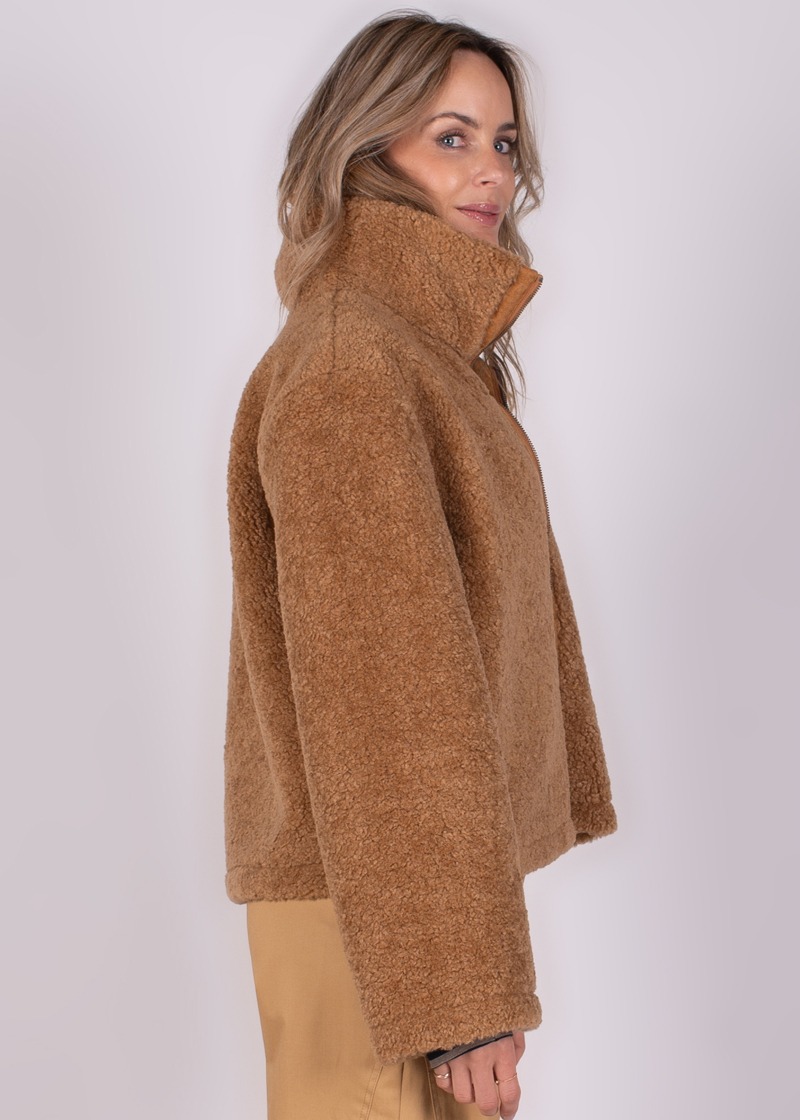 Een model staat zijwaarts, kijkend naar de camera, gekleed in een lichtbruine, pluche Regina jas met opstaande kraag.