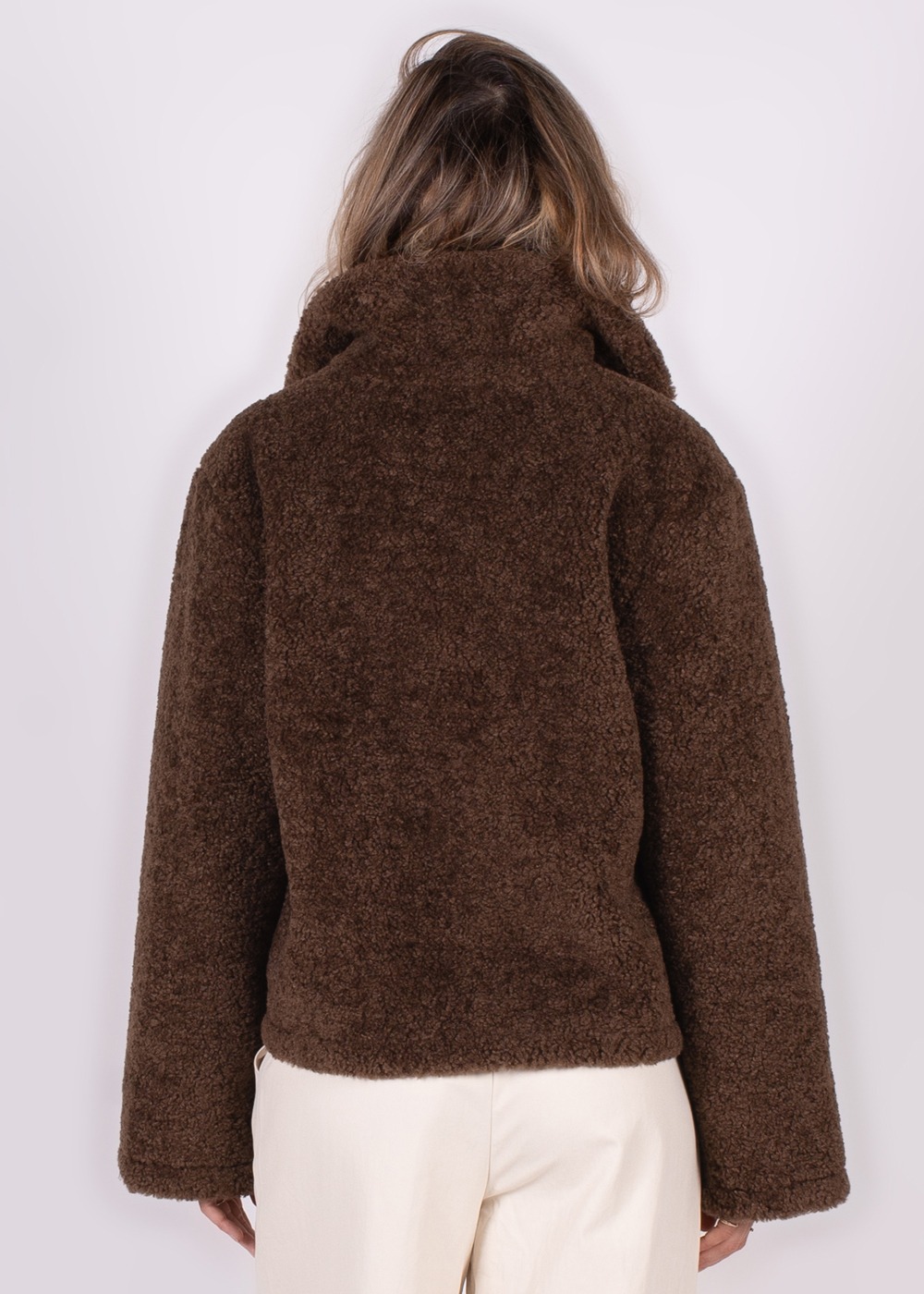 Achteraanzicht van een model dat een donzig, donkerbruin fleecejack draagt met beige broek, weergegeven tegen een neutrale achtergrond.