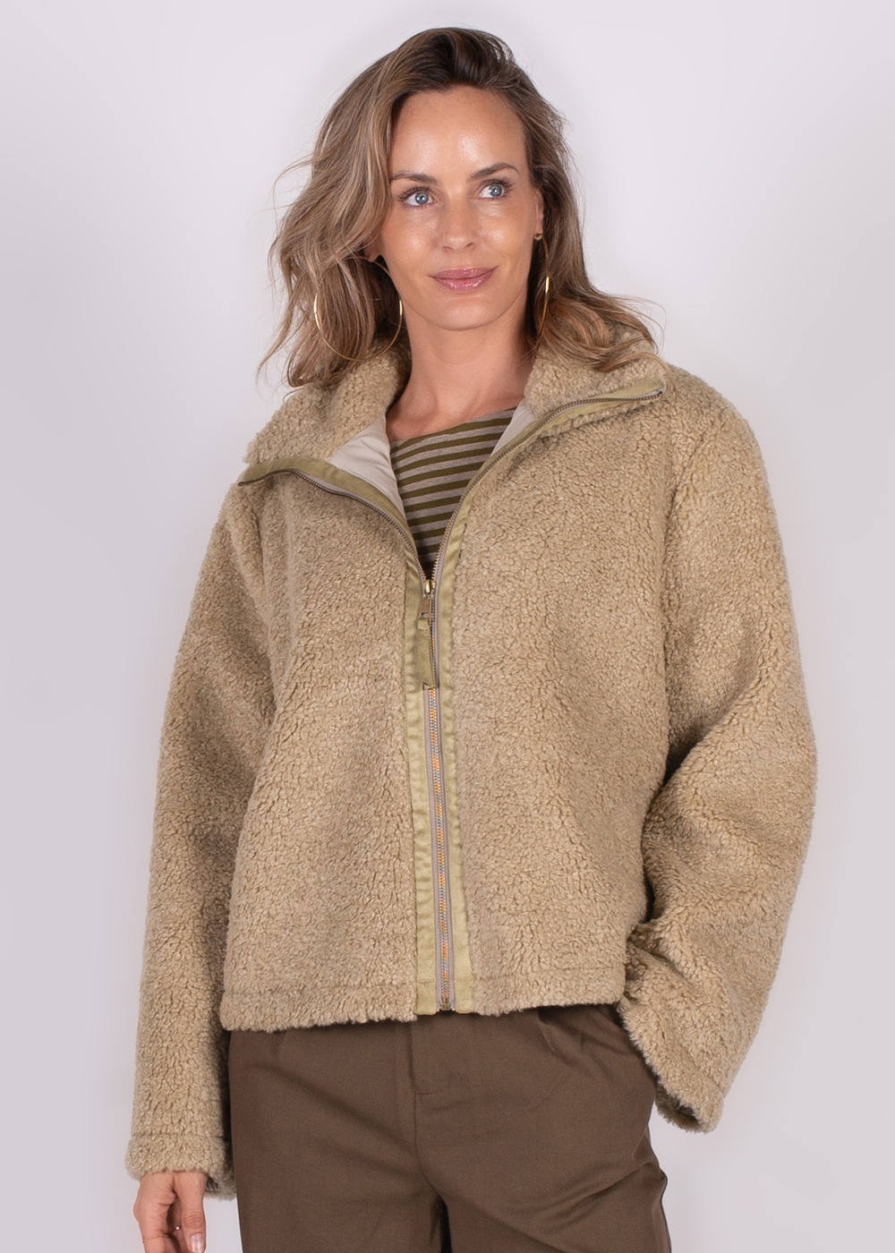 Model draagt een beige teddyjack met rits boven een gestreept shirt.