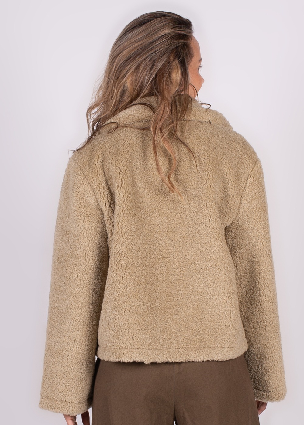 Een vrouw gefotografeerd van achteren, draagt een beige Regina jacket lime-200 met een textuur van schapenvacht.