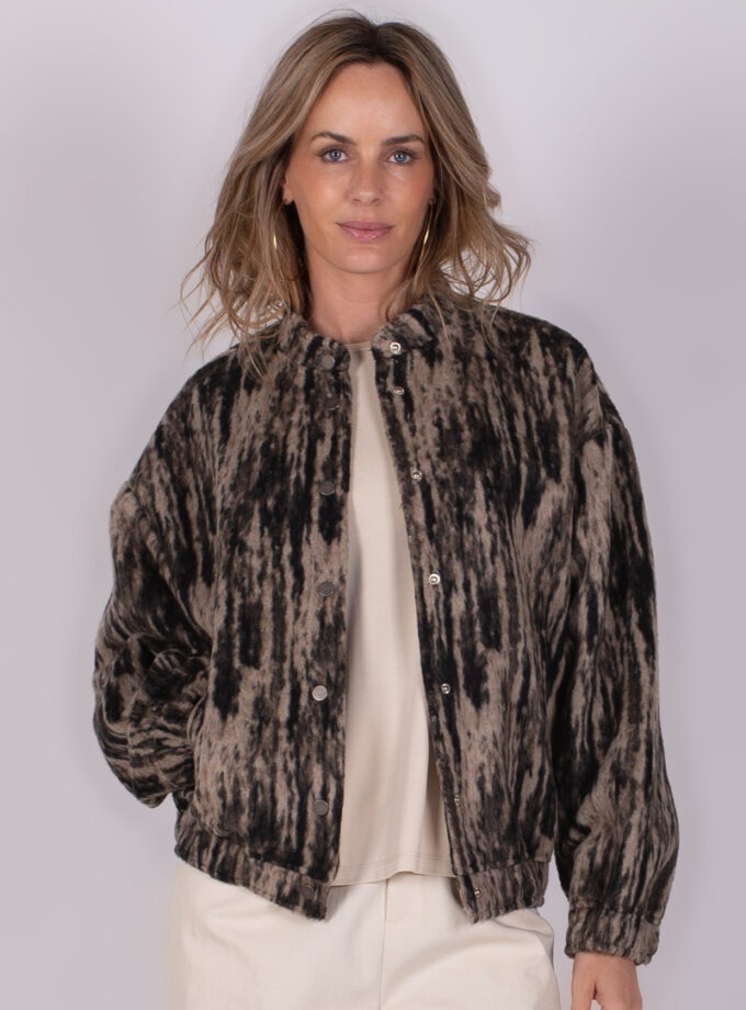 Vrouw in een gevlekt jasje met beige ondergrond, gefotografeerd van voren tegen een neutrale achtergrond.