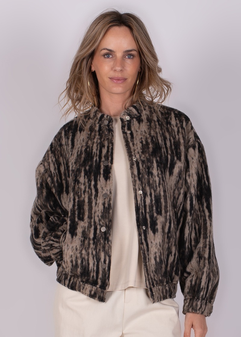 Vrouw in een gevlekt jasje met beige ondergrond, gefotografeerd van voren tegen een neutrale achtergrond.