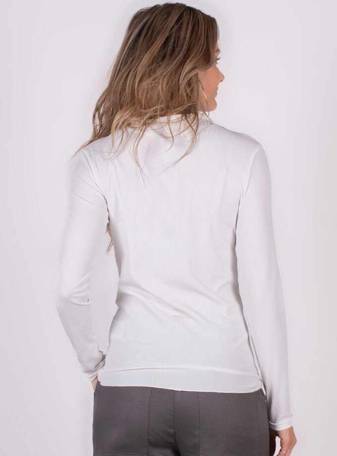 Vrouw in een witte trui met lange mouwen gezien van achteren, met lichtbruin golvend haar en grijze broek.
