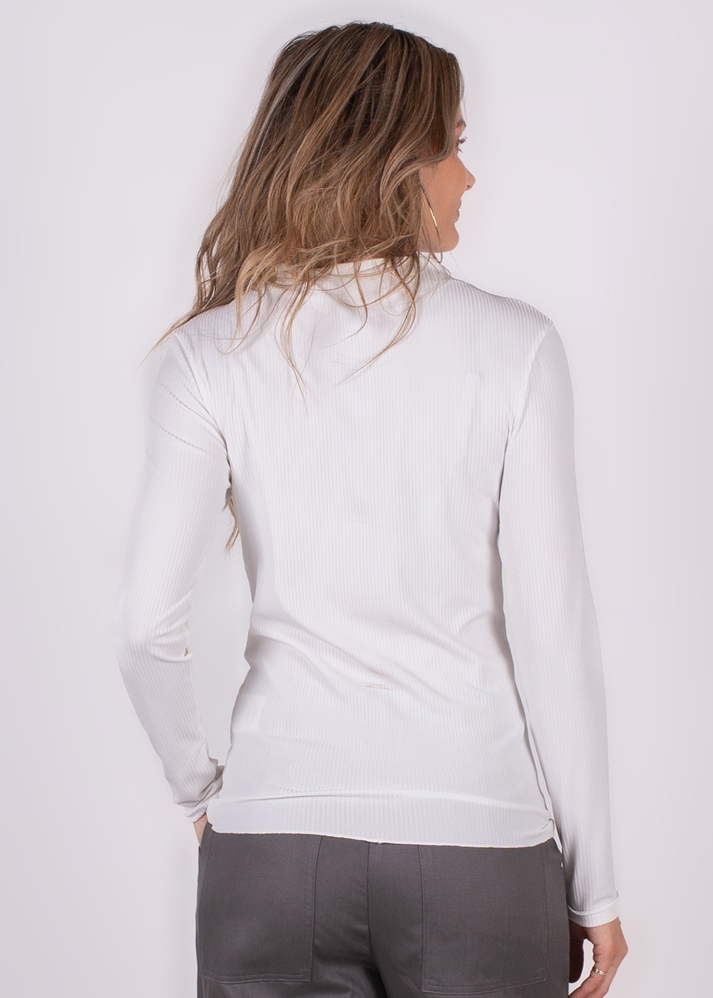 Vrouw in een witte trui met lange mouwen gezien van achteren, met lichtbruin golvend haar en grijze broek.