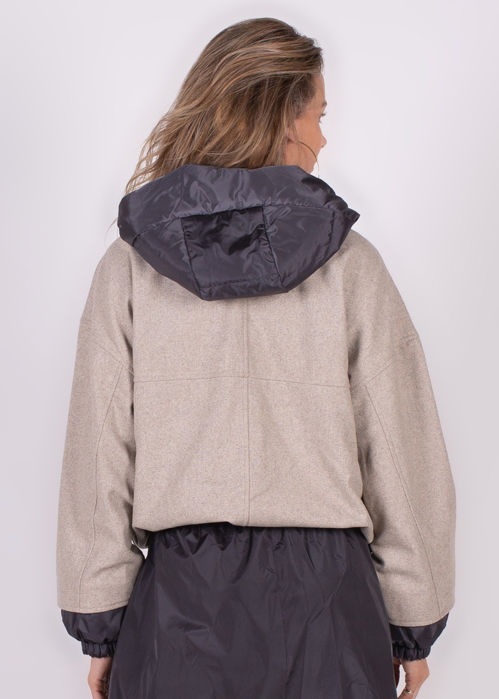 Een vrouw poseert met haar rug naar de camera, terwijl ze een Surat Jacket 414 draagt, met een lichtbruine kleur en een donkere capuchon.