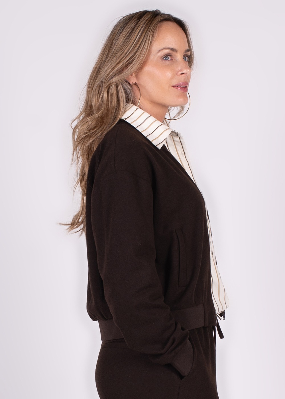 Zijaanzicht van een vrouw met los blond haar die een donkere bomberjack en een gestreepte blouse draagt.