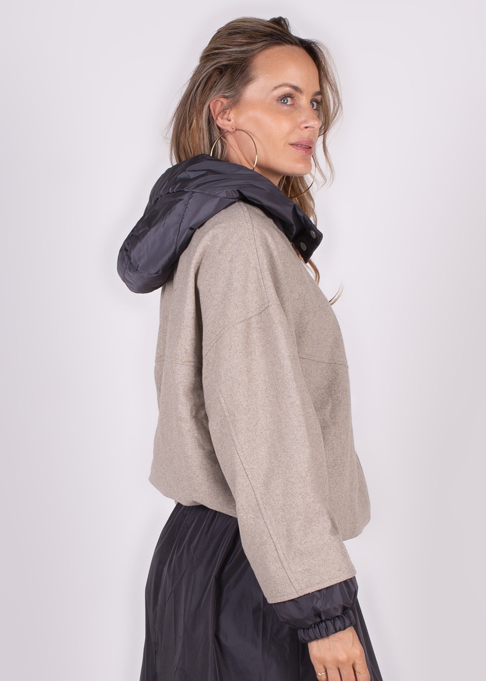 Model draagt een beige Surat jack met een donkergrijze capuchon en zwarte mouwen, zijaanzicht.
