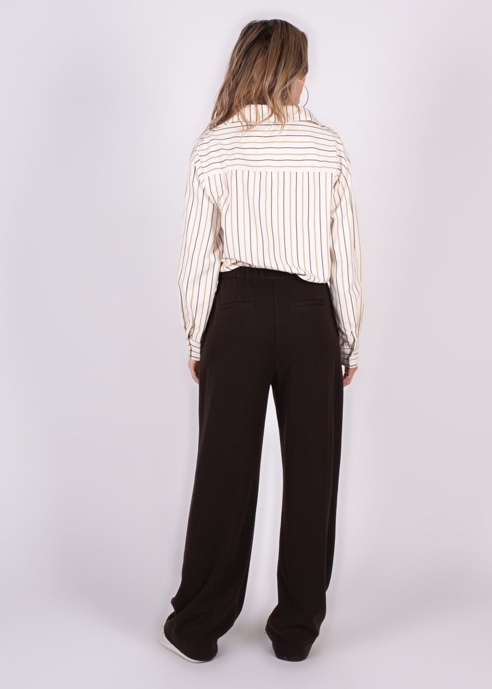 Model draagt een gestreepte blouse en zwarte Surat broek, gezien van achteren.