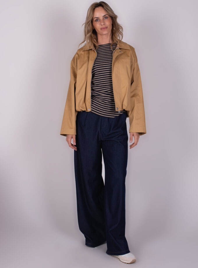 Model draagt een beige Vienna jack over een gestreept shirt en wijde donkerblauwe broek, tegen een neutrale achtergrond.