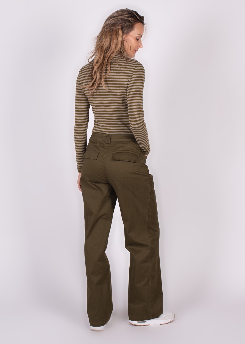 Een vrouw met lang haar, gezien van achteren, draagt een gestreepte coltrui en olijfgroene Vienna pant moss-broek.