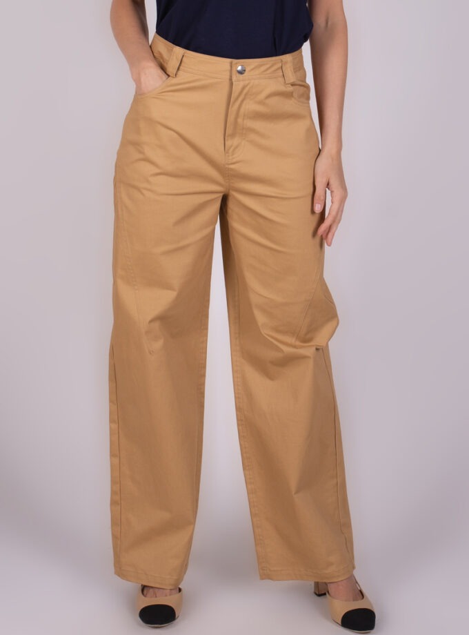 Model draagt beige wijde Vienna broek, gezien van voren tot aan de enkels, gecombineerd met een donkerblauw shirt.