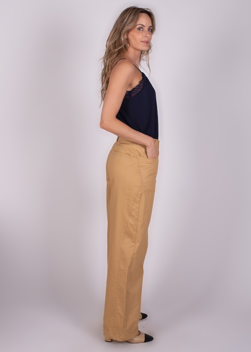 Een vrouw in zijaanzicht draagt beige Vienna-broek met een donkerblauwe top en beige schoenen.